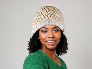 Woman with curly natural hair wearing a beige satin lined winter hat with a white faux fur trim.