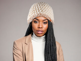 Woman with braids wearing a cream satin lined winter hat with a brown and white faux fur trim.
