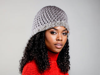 Woman wearing a gray satin lined winter hat with a gray faux fur trim.