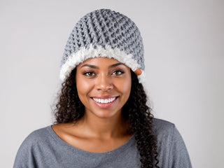 Woman wearing a slate satin lined winter hat with a white faux fur trim.