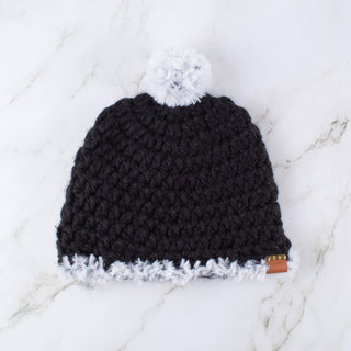 Black satin lined winter hat with a white faux fur pom and faux fur trim.