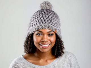 Woman wearing a gray satin lined winter hat with a gray faux fur pom and trim.