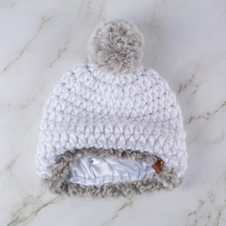 White satin lined winter hat with a gray faux fur trim and pom.