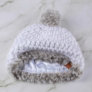 White satin lined winter hat with a gray faux fur trim and pom.